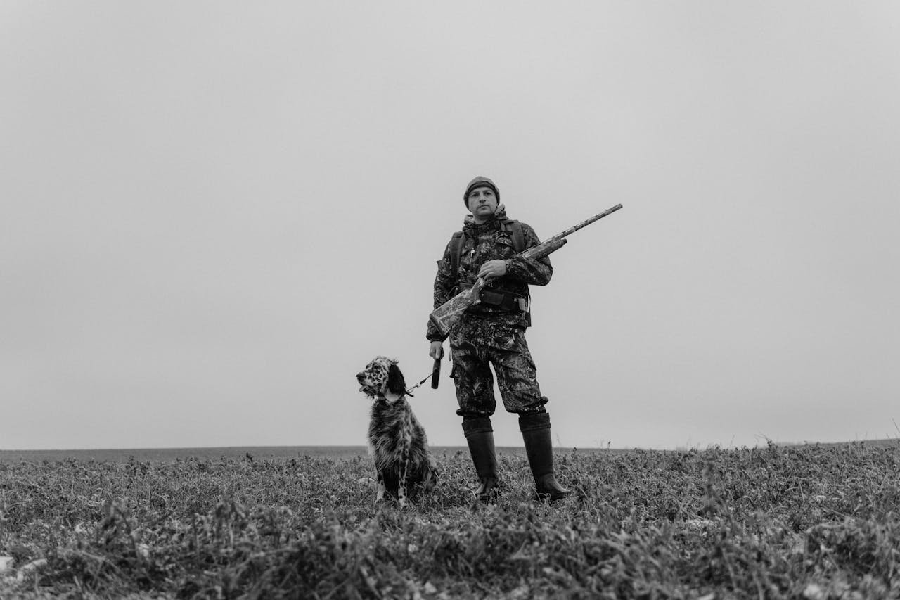 A hunter and his dog stand in a field in grayscale, creating a classic look.